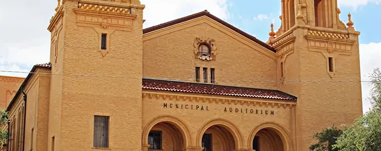 Historic tan brick municipal auditorium with twin towers and arched entranceways.