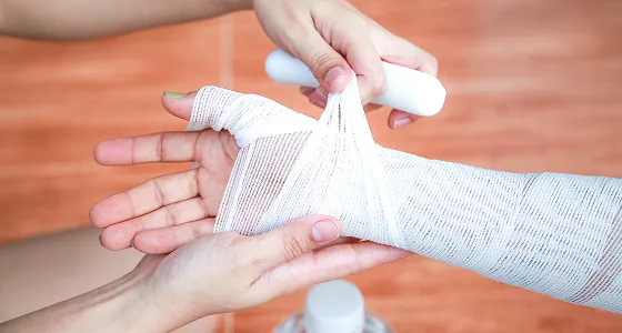 Person wrapping a white elastic bandage around another person's forearm and hand.