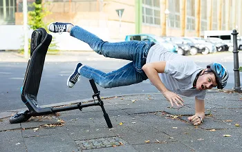 Young man wearing helmet falling off electric scooter on pavement outdoors.