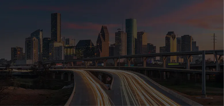 Panoramic view of a city skyline at dusk with illuminated highways and light trails.