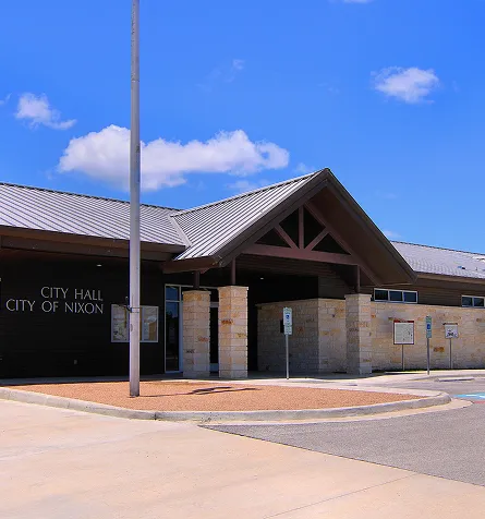 Exterior view of City Hall building of Nixon with stone pillars and metal roof under blue sky.