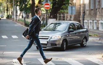 Man in business attire crossing street at pedestrian crosswalk with car and no entry sign.