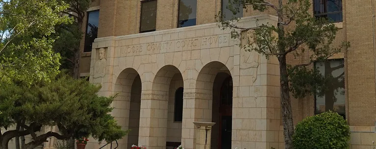 Exterior view of Moore County Courthouse with beige stone arches and surrounding greenery.