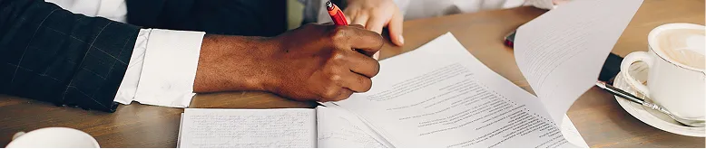 Two individuals reviewing and annotating printed documents at a wooden table.