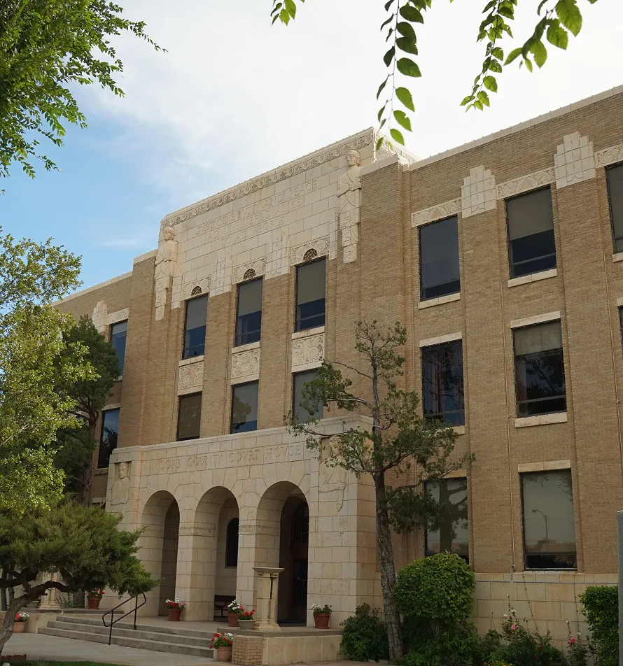 Exterior view of a three-story tan brick courthouse with arched entrance and decorative stonework.