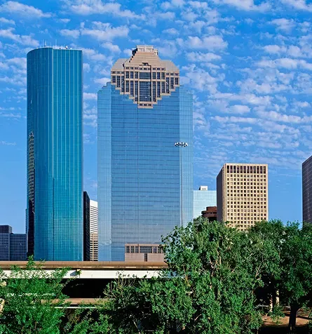 City skyline featuring modern glass skyscrapers under a partly cloudy blue sky.