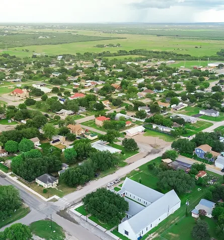 Aerial view of a suburban neighborhood with houses, trees, and open green fields.