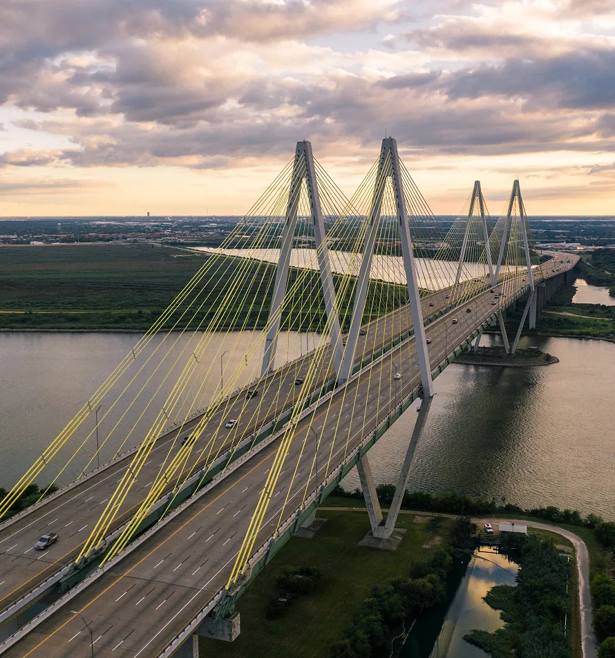 Aerial view of a cable-stayed bridge with yellow suspension cables over a river at sunset.