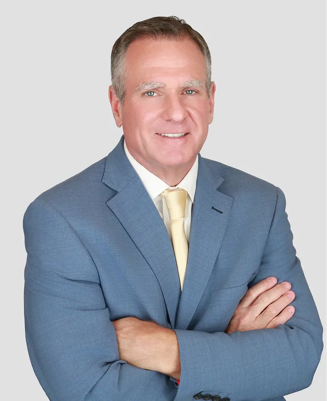 Middle-aged man in blue suit and yellow tie, smiling with arms crossed.