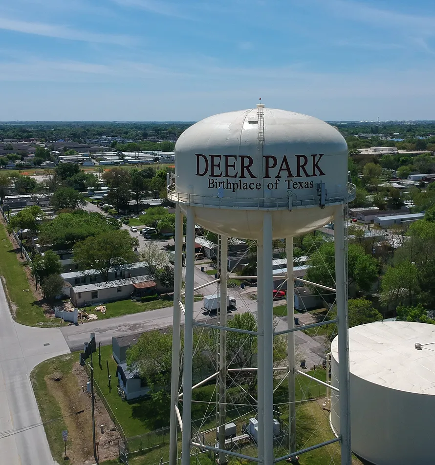 Aerial view of a white water tower labeled "DEER PARK Birthplace of Texas" above residential neighborhood.