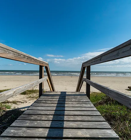 Wooden boardwalk leading to sandy beach under clear blue sky.