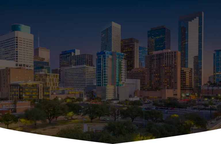 Downtown city skyline at dusk with illuminated modern skyscrapers and foreground park area.