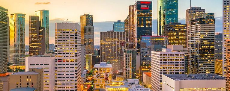 Panoramic view of a city skyline at sunset with illuminated office buildings.