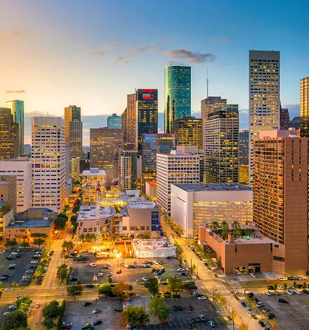 Aerial view of a city skyline at dusk with illuminated skyscrapers and streets.