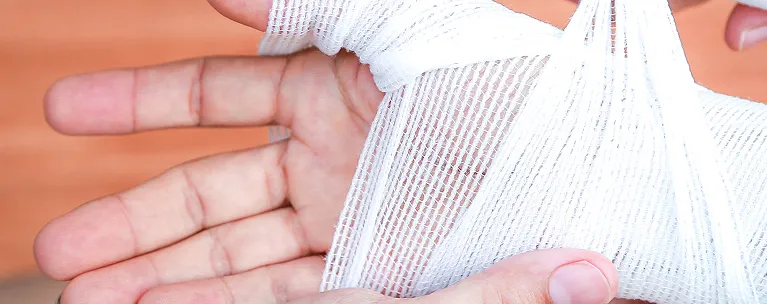 Close-up of a hand being wrapped with white medical gauze bandage.