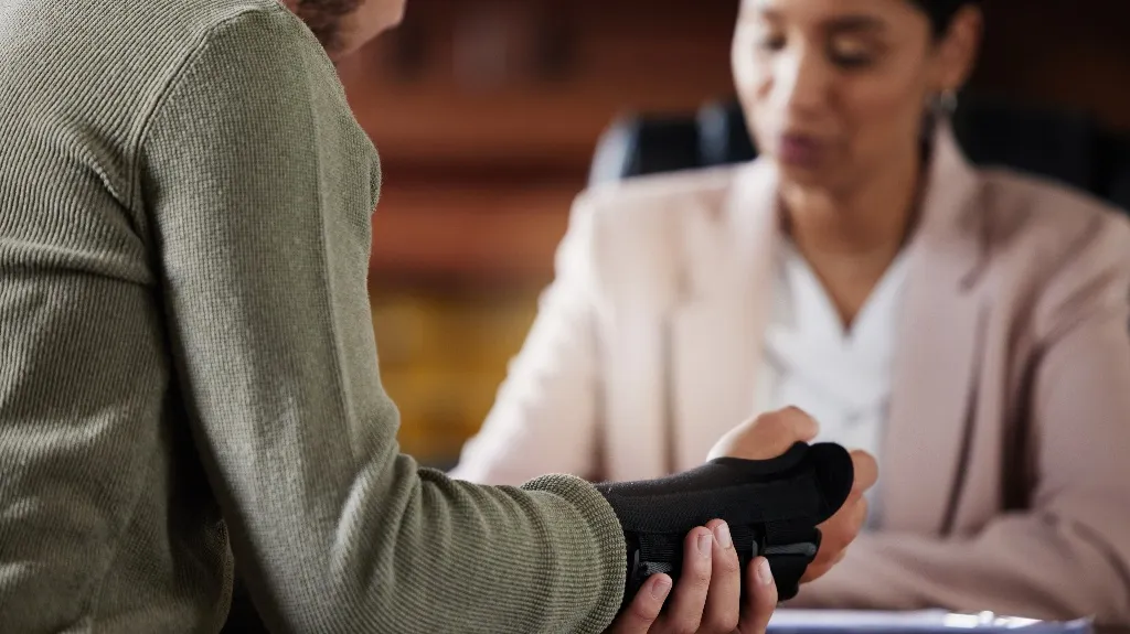 Person wearing a wrist brace is consulting a professional in a light pink blazer.