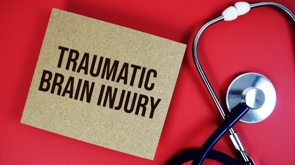 Brown cardboard with "Traumatic Brain Injury" text beside a black and silver stethoscope on red background.