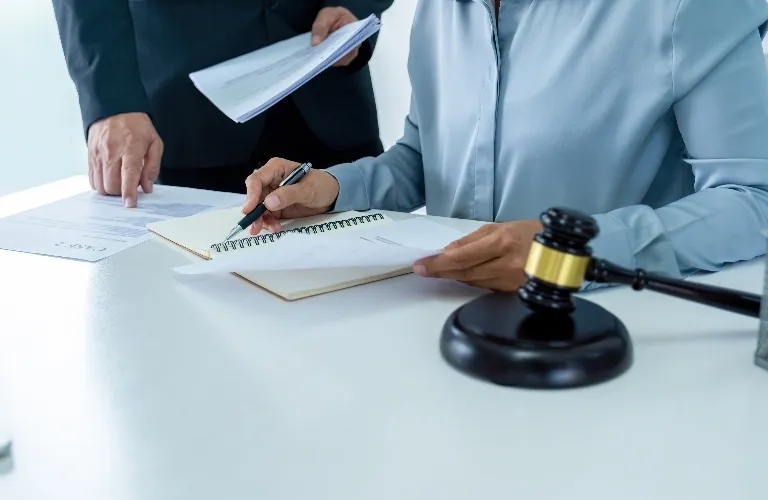 Two professionals reviewing documents at a white desk with a black and gold gavel.