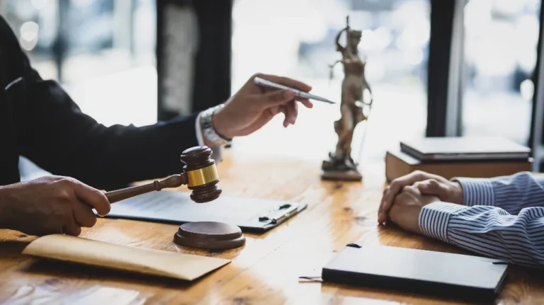 Two people at a wooden desk with a judge's gavel, legal books, and a Lady Justice statue.