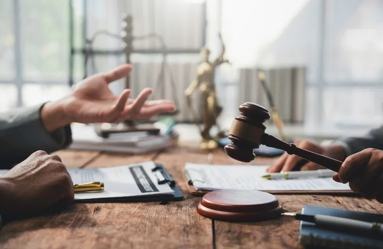 Two individuals at a wooden table, one holding a judge's gavel, legal documents and a Lady Justice statue in the background.