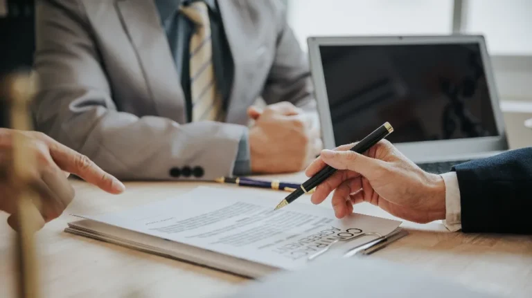 Two professionals in suits reviewing a contract agreement document at a wooden desk.