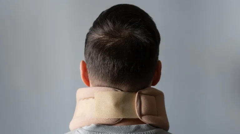 Rear view of person wearing a beige neck brace against a plain gray background.