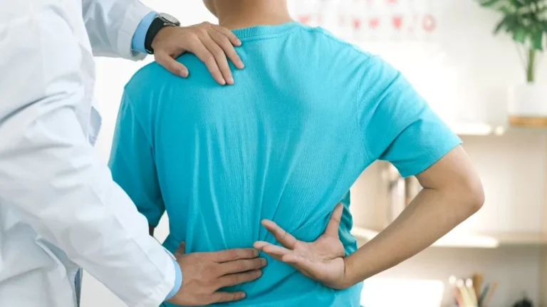 Medical professional examining patient's lower back, patient wearing bright blue shirt.