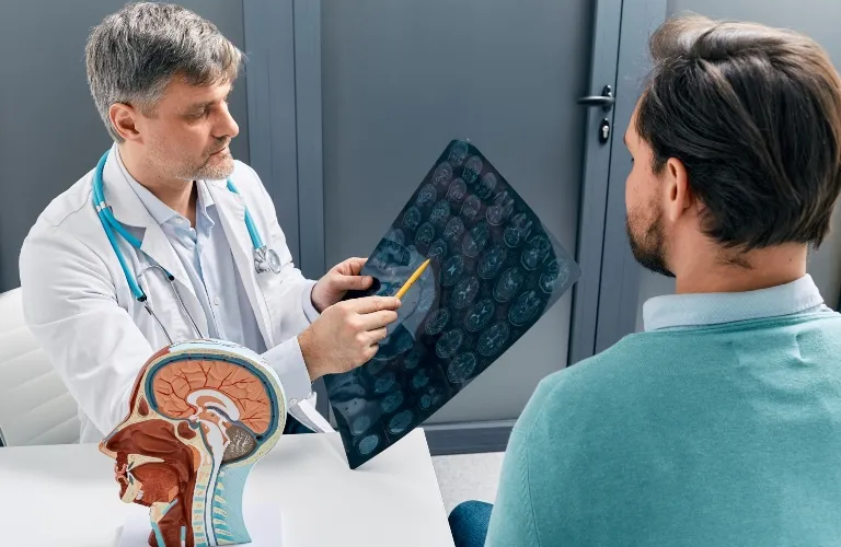 Doctor in white coat with stethoscope examining brain scan with patient in teal sweater.