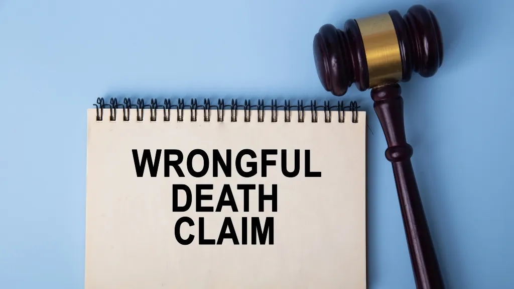 Notepad with "Wrongful Death Claim" text and a wooden judge's gavel on a blue background.