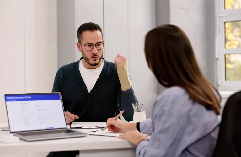 Two professionals in an office discussing a health insurance claim, with a laptop and documents.