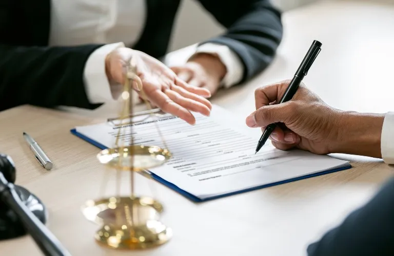 Two professionals reviewing and signing a legal document at a desk with scales of justice.