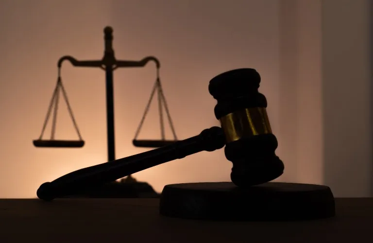 Dark silhouette of a wooden judge's gavel and scales of justice against a warm background.