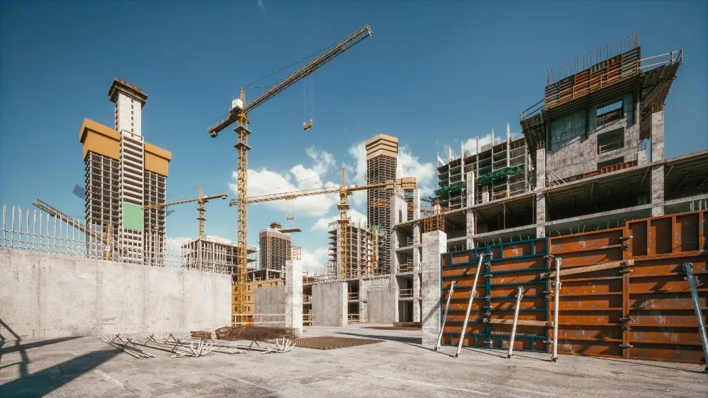 Construction site with multiple concrete buildings and yellow tower cranes under clear blue sky.