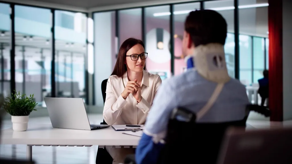 Professional woman in white blouse consulting injured man with neck brace in modern office.