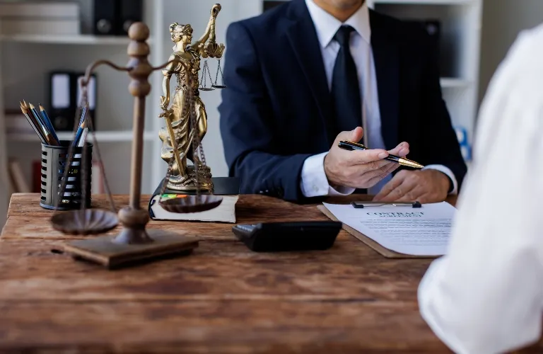 Man in suit discussing contract at wooden desk with Lady Justice statue and scales of justice.