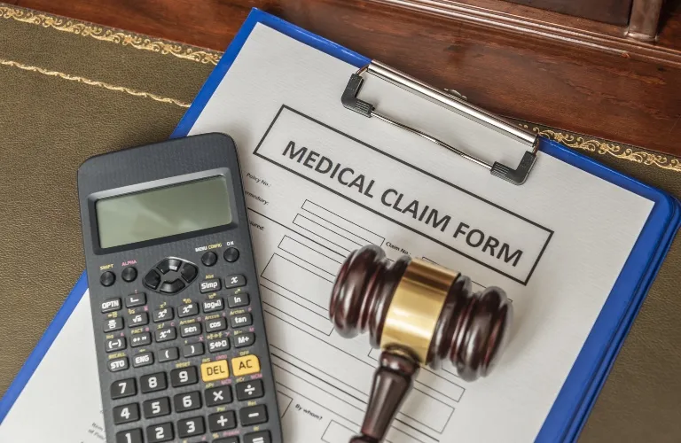 Clipboard with medical claim form, calculator, and wooden gavel on desk.